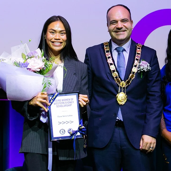 Man and woman standing on stage during an award presentation, with one person holding a certificate and flowers.