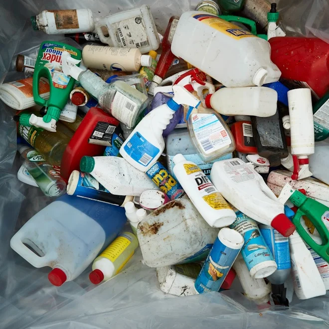 A collection of mixed plastic bottles and containers, including detergents and cleaning products, piled in a recycling bin, conveying environmental awareness.