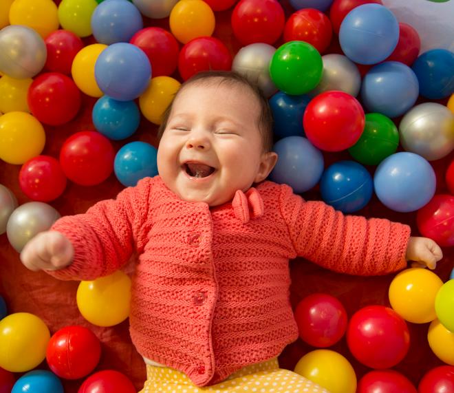 Baby laughing laying in pit of colouful balls