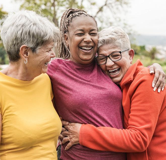 Three elderly women hugging and smiling